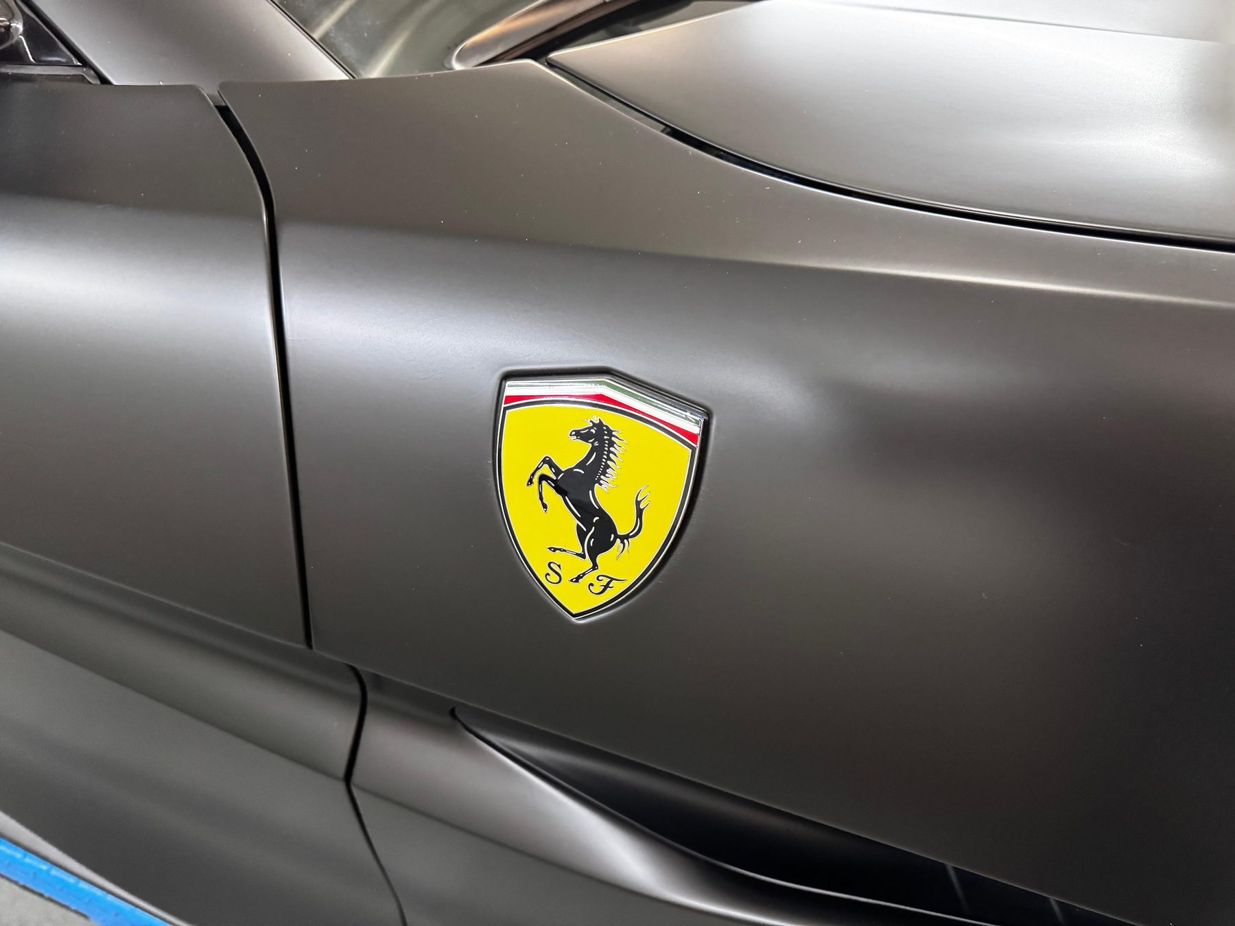 Nahaufnahme einer Ferrari-Plakette nach einer Vollfolierung in Mattschwarz – präzise verklebte Kante bei STARK Folientechnik
